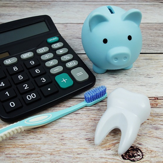 Calculator, piggy bank, toothbrush, and model tooth on wooden surface