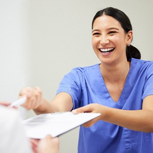 Woman in blue scrubs handing pen and paperwork to patient