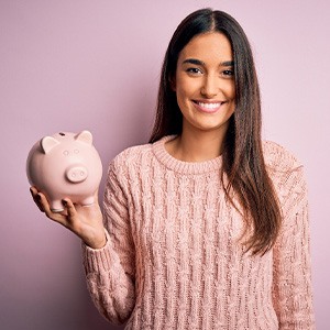 Woman in pink sweater holding piggy bank with pink background