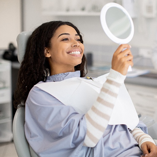 Woman smiling at reflection in handheld mirror